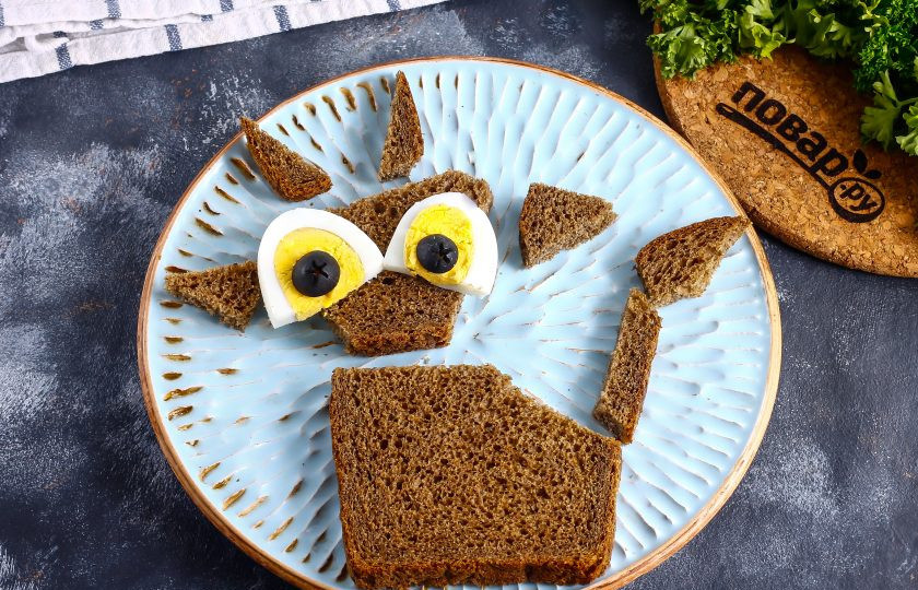 1. Этап. Бутерброд Веселый Бычок: Отварное куриное яйцо очистите от скорлупы, промойте в воде и нарежьте кружочками вертикально. Аккуратно отделите два из них с желтком и срежьте нижние края. Маслины без косточек разрежьте горизонтально пополам, чтобы получились зрачки и ноздри. Хлеб нарежьте так, как показано на фото: голова, туловище, хвост, кисточка хвоста, уши и рога.