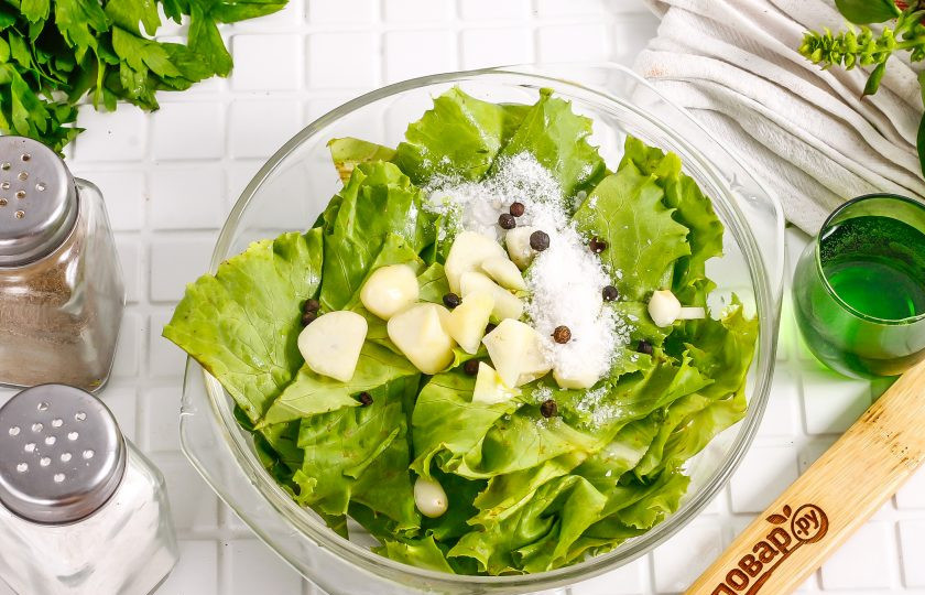 1. Этап. Маринованные листья салата с чесноком и уксусом: Очистите зубчики чеснока, промойте их в воде, нарежьте слайсами. Всыпьте в емкость к салату вместе с солью, горошинами черного перца.