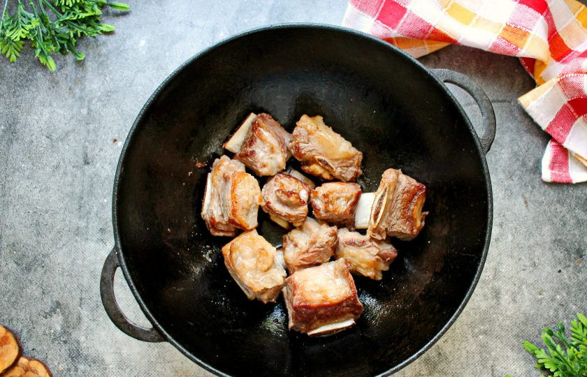 1. Этап. Говяжьи ребрышки в казане с луком: Поставьте казан на сильный огонь и влейте растительное масло, разогрейте. Говяжьи ребрышки разрежьте на части и выложите в казан. Обжарьте их до золотистого цвета со всех сторон, перемешивая.