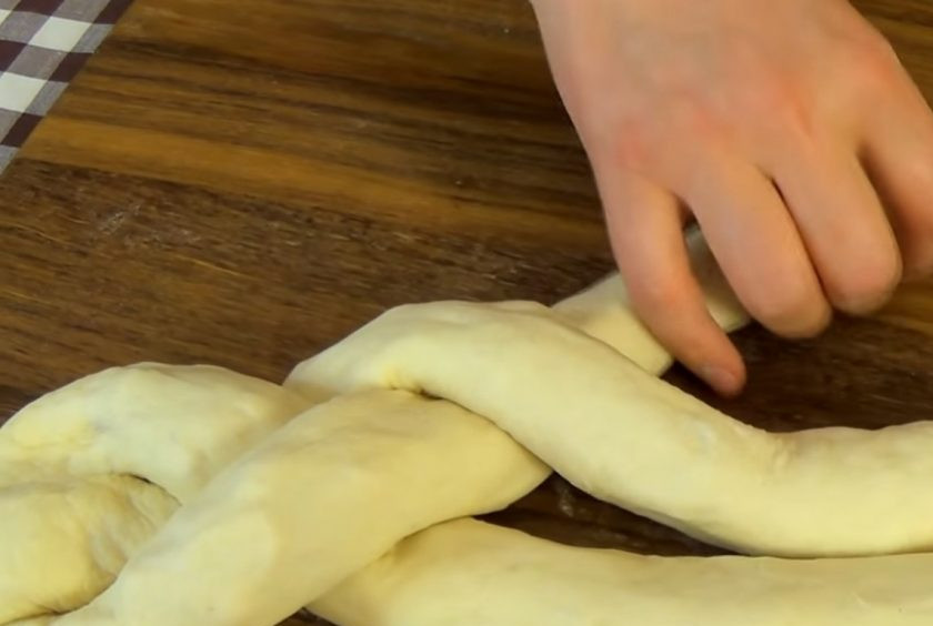 1. Этап. Хлебная коса с начинкой: 4. Каждый рулет слегка растяните, положите швом вниз и скрепите одни края вместе. Сплетите косу и подверните края. Перенесите косу на бумагу для выпечки, смажьте взболтанным яйцом и посыпьте семенами.