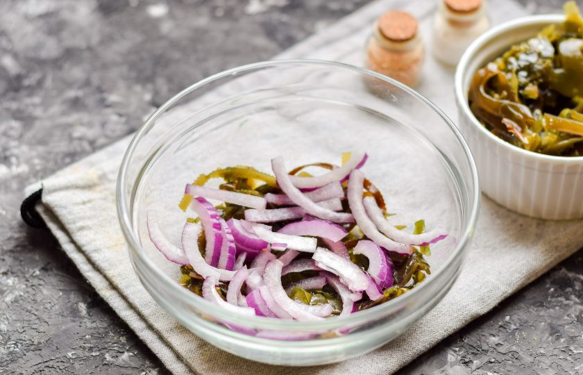 1. Этап. Салат Морское дно с морской капустой: Красный лук очистите и нарежьте полукольцами, выложите лук поверх капусты.