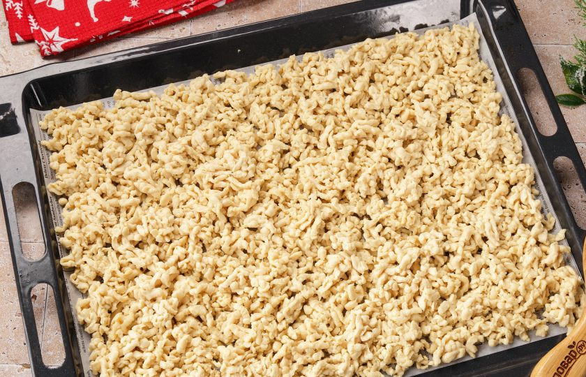 1. Этап. Новогодний торт Зеленая Змея: Натрите тесто на тёрке и выложите тонким слоем на застеленный пергаментом противень. Выпекайте около 15-20 минут при температуре 180 градусов. Периодически поглядывайте.