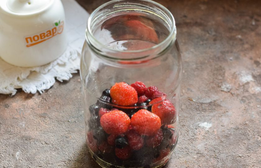 1. Этап. Компот из клубники, малины и смородины на зиму: Банку для заготовки тщательно вымойте с пищевой содой, после ополосните хорошо под теплой проточной водой. Стерилизуйте банку удобным способом – над паром, в духовке или микроволновке. Крышку опустите в воду и проварите 10 минут. Переложите в банку ягоды.