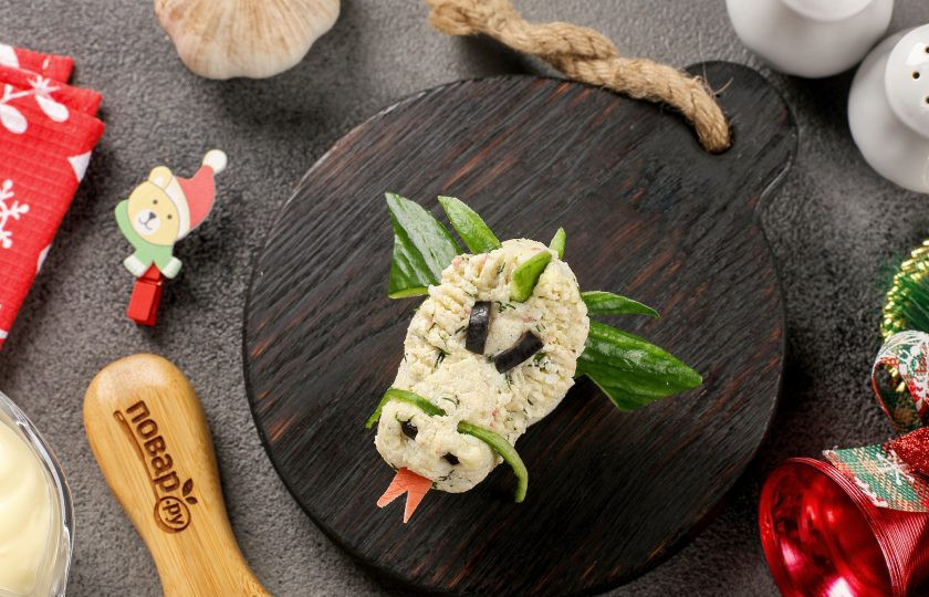 1. Этап. Фаршированные яйца Новогодние драконы: Из отрезанной красной части крабовой палочки вырежьте язык. Глаза и ноздри сделайте из маслин. Из огурца так же можно вырезать уши, шипы и усы дракона. На каждую фаршированную половинку яйца установите голову, а под ней крылья дракона. По желанию, вооружившись зубочисткой можно придать рельеф на поверхности фигуры.