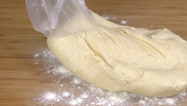 1. Этап. Хлеб на сковороде: 3. Выкладываем тесто на присыпанную мукой поверхность. Сверху просеиваем оставшуюся муку. Начинаем замешивать руками. Затем готовое тесто перекладываем в целлофановый пакет и даем ему постоять полчаса. После чего обратно выкладываем на чуть присыпанную мукой поверхность.