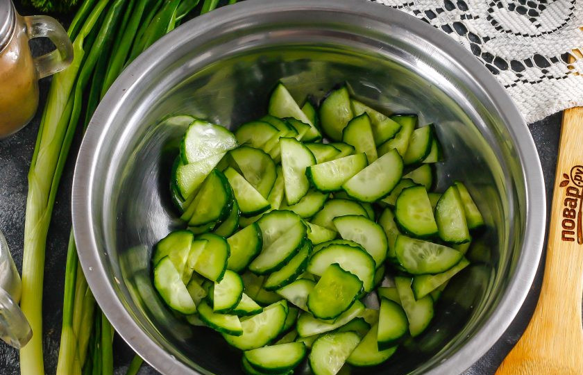 1. Этап. Салат с морской капустой и свежим огурцом: Нарежьте огурцы полукольцами и высыпьте нарезку в глубокую емкость.
