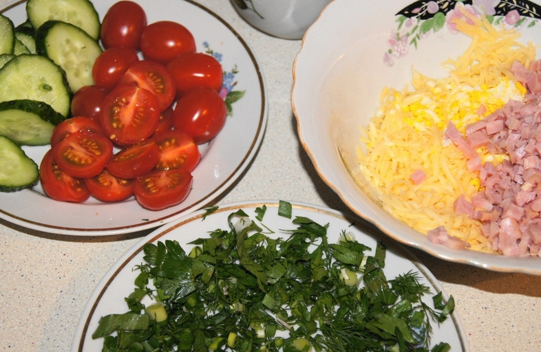 1. Этап. Закуска Мухоморчики: Помидоры режем на половинки, огурцы — колечками. Всю зелень измельчаем. Вареные яйца и сыр трем на мелкой терке, а колбасу режем кубиками.