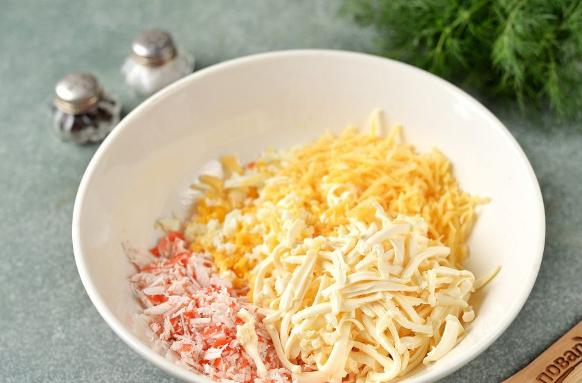 1. Этап. Новогодняя закуска Кролики на крекерах: Почистите яйцо от скорлупы, снимите упаковку с крабовых палочек и плавленого сырка. Натрите все эти ингредиенты, выложите в глубокую миску. Также натрите остатки твердого сыра, который остался от ушек.