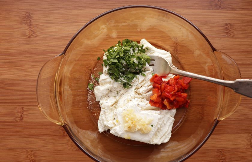 1. Этап. Кальмары с творогом: Приготовьте творожную начинку. Разомните творог вилкой, добавьте нарезанную петрушку и сладкий перец, измельченный чеснок, соль и молотый черный перец по вкусу, перемешайте.