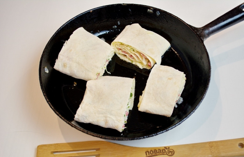 1. Этап. Жареный лаваш с колбасой и сыром: Сковороду разогрейте хорошо. Капните в сковороду немного растительного масла. Нарезанный лаваш выложите в сковороду и обжарьте с двух сторон.