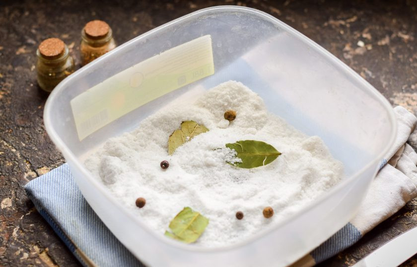 1. Этап. Сало засоленное: После возьмите удобный контейнер, в котором будет солиться сало. Всыпьте в контейнер половину порции соли, добавьте лаврушку и перцы.