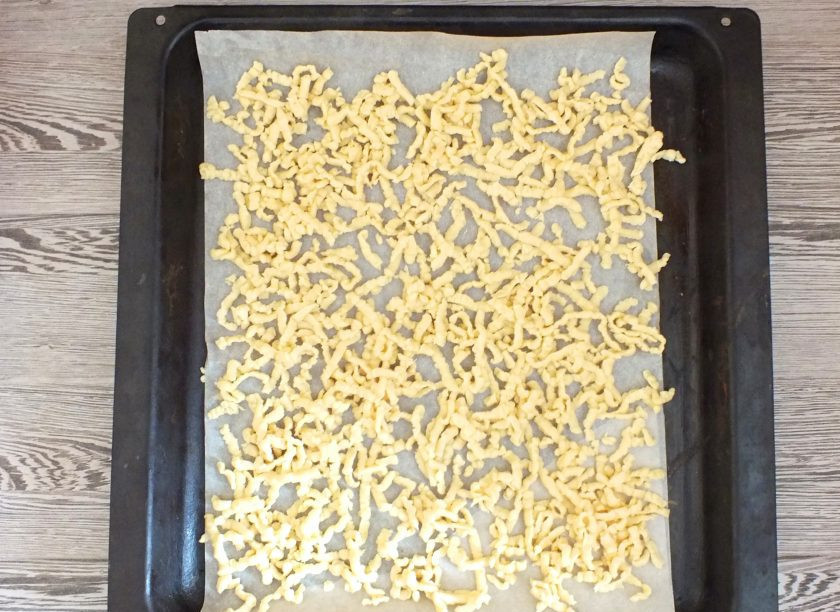 1. Этап. Торт Муравейник без сметаны: Достаньте тесто из морозилки. Разделите на две части. Противень застелите бумагой. Возьмите одну часть и натрите ее на терке на противень. Натирайте на весу, равномерно распределяя, чтобы не образовывались 