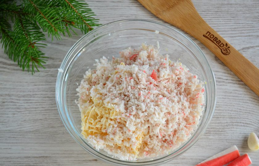 1. Этап. Закуска на год Крысы: Крабовые палочки натрите на мелкой терке. Половину натертой массы добавьте к сырно-яичной массе, а вторую половину пересыпьте в отдельную тарелочку. Красную часть одной крабовой палочки отложите, она нам понадобится для украшения. Также оставьте половину одной палочки, ее используем для ушек.