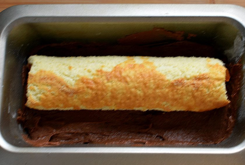 1. Этап. Рулет в кексе «Апельсиновый блюз»: Выложите немного теста в длинную форму для кекса. Сверху выложите рулет, предварительно обрезав его по размерам формы.