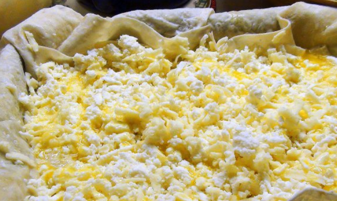 1. Этап. Ачма с сыром и творогом: Вливаем 2 ст.л. растопленного масла и обильно присыпаем сыром (творог+ сулугуни). Поливаем еще раз маслом и вливаем пол стакана кефира с яйцами.