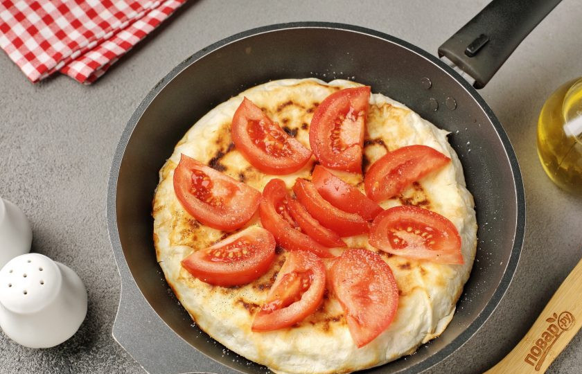 1. Этап. Яичница с помидором и сыром в лаваше на сковороде: Сверху выложите нарезанный дольками помидор. Посолите и поперчите по вкусу.