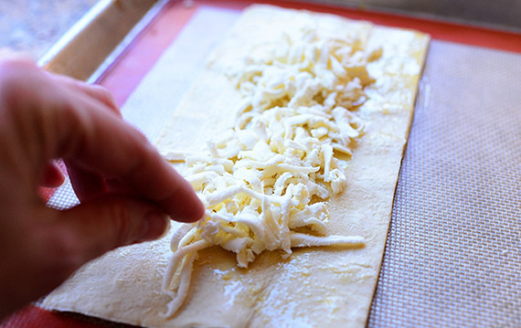 1. Этап. Слоеная пицца с грибами: Тесто смажьте маслом и выложите тертый сыр.