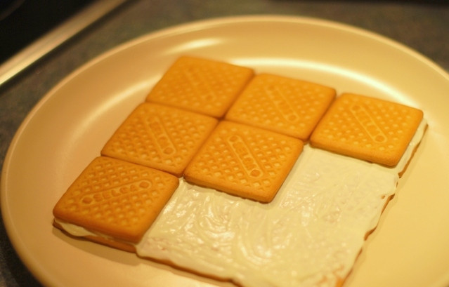 1. Этап. Творожный торт из печенья: На плоском блюде начните сборку торта: первые два слоя (можно и первые три) смазывайте сметаной с сахаром. Оставьте сметану для финальной обмазки торта.