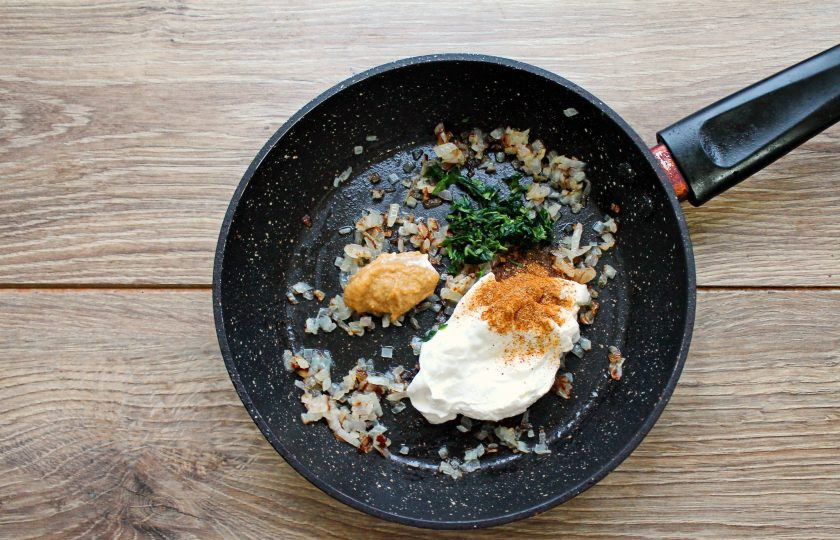 1. Этап. Рулет из индейки с яйцом в духовке: Добавьте в сковороду с луком сметану, горчицу, специи и резаную зелень. Все посолите, поперчите и перемешайте.