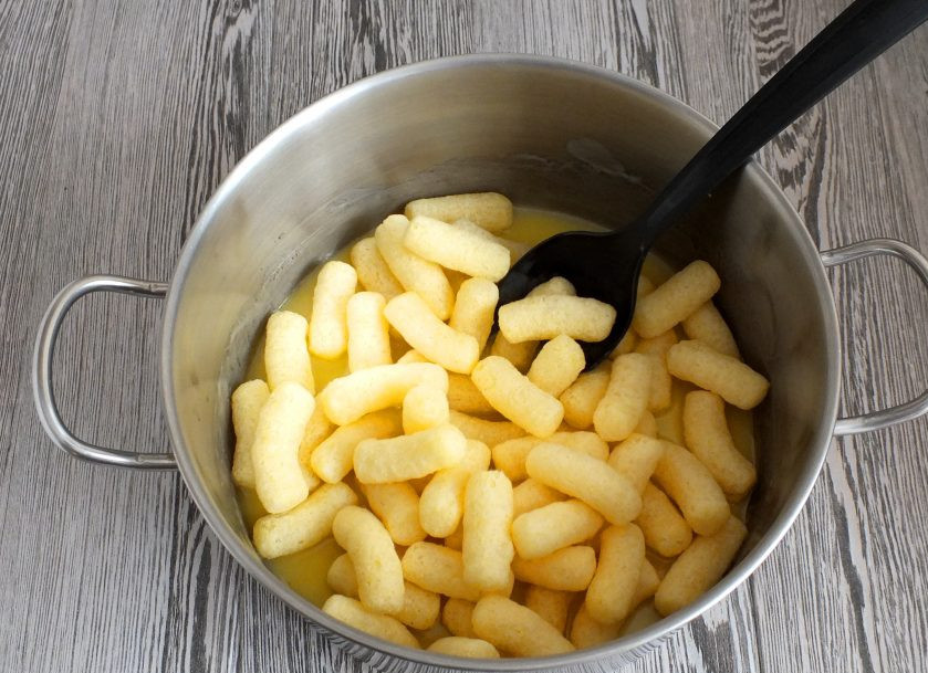 1. Этап. Чак-чак из кукурузных палочек: Всыпьте кукурузные палочки. Аккуратно размешайте, чтобы каждая палочка была покрыта масляной массой.