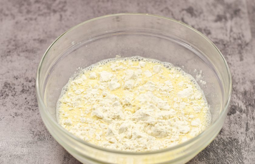 1. Этап. Блины на молочной сыворотке без дрожжей: Просейте пшеничную муку в миску с основой теста. Перемешайте все, чтобы не было комочков.