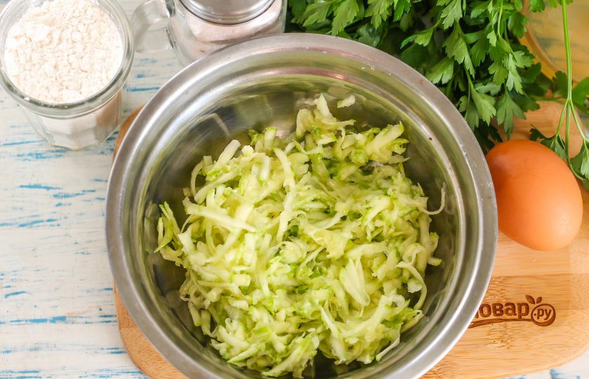 1. Этап. Кабачковые оладьи с колбасой: Кабачок промойте в воде, срежьте с плода хвостики и натрите его на терке в глубокую емкость. Посолите и оставьте на 5 минут, чтобы нарезка выделила жидкость. Обязательно отожмите кабачковую массу, сливая сок.