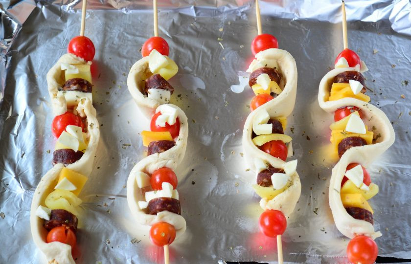 1. Этап. Пицца на шпажках в духовке: Выложите заготовки на противень, застеленный фольгой. В отдельной миске смешайте оливковое масло с итальянскими травами (при желании можно немного присолить), полученной смесью сбрызните пиццу на шпажках. Затем сверху выложите измельченную моцареллу. Ее можно натереть на крупной терке, а можно просто мелко нарезать, как это сделала я. Запекайте пиццу на шпажках в духовке примерно 20-25 минут, пока тесто не вырастет и не подзолотится.