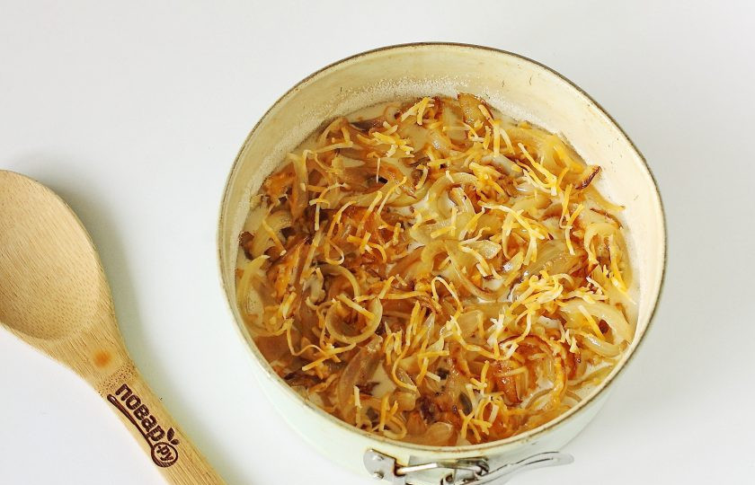 1. Этап. Заливной луковый пирог: Форму для запекания смажьте маслом, дно и бока обсыпьте мукой или манкой. Вылейте половину порции теста и равномерно разложите начинку.