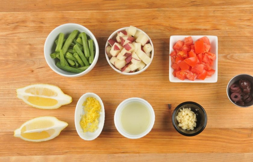 1. Этап. Жареная форель с гарниром: 1. Подготовьте ингредиенты. Нарежьте небольшими кубиками помидор и картофель. Оливки нарежьте кружками. Чеснок измельчите. Фасоль разделите на половинки. С половины лимона натрите цедру и выжмите сок, вторую часть разрежьте на 2 дольки.