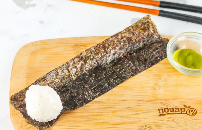 1. Этап. Гунканы: Слегка сплющите шарик риса и выложите его на край листа нори. Обверните водоросли вокруг рисовой начинки. Должны получиться овальные лодочки. Подрежьте нори, если край получится неровным.