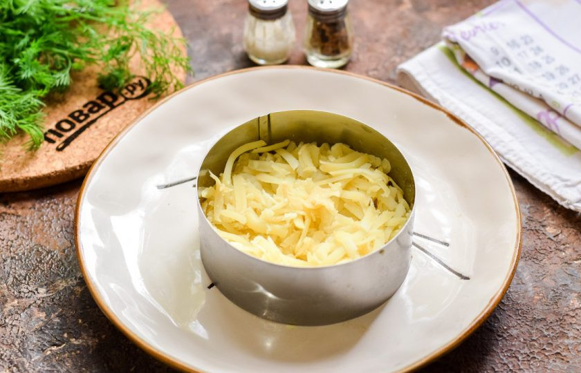 1. Этап. Салат Мимоза на Новый год Быка 2021: Подготовьте кулинарное кольцо, с его помощью будет легко и просто собрать салат. Картофель натрите на средней терке и выложите первым слоем. Все слои салата смажьте майонезом, посолите и поперчите по вкусу.