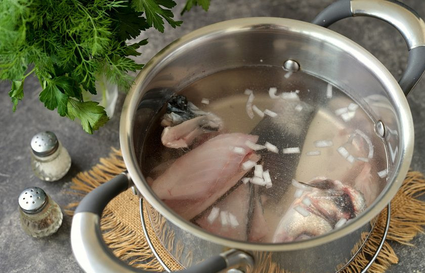 1. Этап. Уха из сибаса: В кастрюлю на 2,5 литра выложите голову, хвост, хребет и кости сибаса. Добавьте нарезанный мелко репчатый лук, налейте воду и варите бульон на тихом огне минут 15.