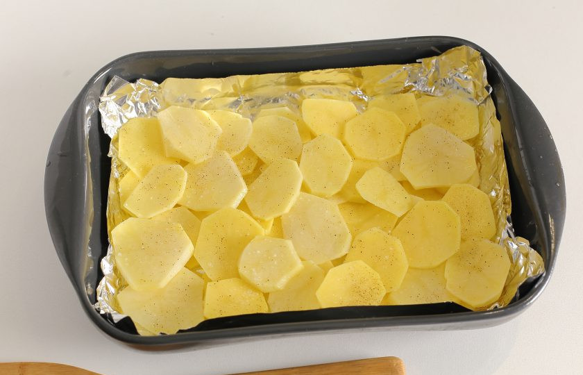 1. Этап. Картофель запеченный с говяжьей печенью в сметане: Форму для запекания смажьте маслом (я предварительно застилаю еще форму фольгой). Картофель нарежьте тонкими кружочками и разделите на две части. Часть картофеля выложите в жаропрочную форму, оставляя небольшое количество для второго слоя. Картофель слегка присыпьте перцем и солью. Добавляя соль, учтите, что картофель будет заливаться уже соленой подливой, поэтому не переборщите с этой специей.