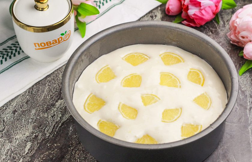 1. Этап. Бисквитный пирог с лимоном: Смажьте форму растительным маслом и разогрейте духовку до 180 градусов. Выложите тесто в форму. Оставшуюся часть лимона нарежьте полукольцами, удаляя косточки. Главное — ломтики должны быть тонкими. Выложите нарезку сверху на тесто.