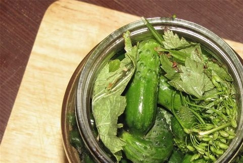 1. Этап. Маринованные корнишоны: На дно горячей банки уложите половину листьев и зонтик укропа. Вплотную уложите огурцы и сверху заложите их оставшимися листьями с укропом.