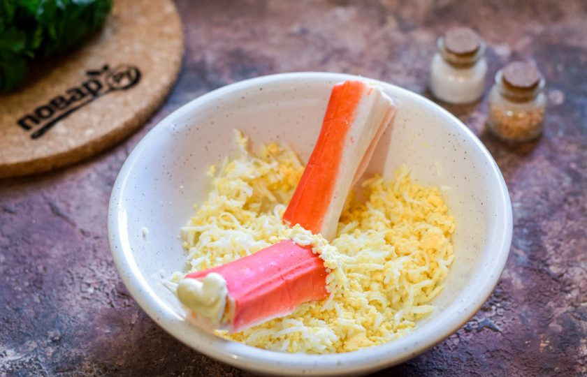 1. Этап. Крабовые палочки Очаровашки: Сверните палочки трубочками, края палочек смажьте майонезом и щедро засыпьте натертыми яйцами, чтобы получилась 