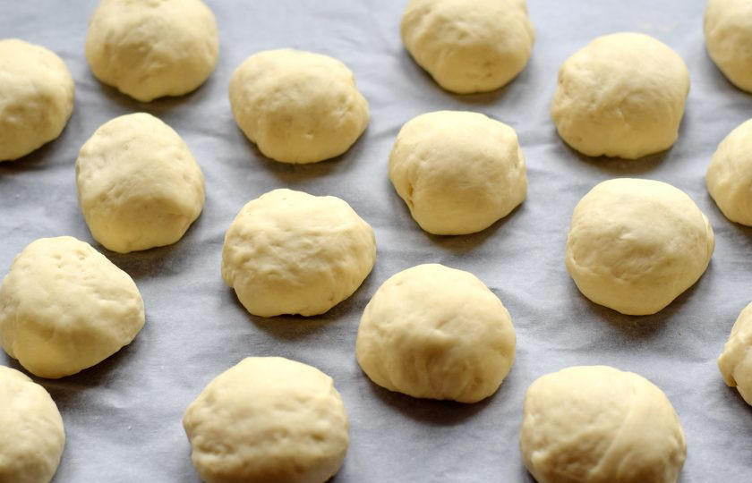 1. Этап. Булочки Столичные: Через час тесто перемешайте, разделите на равные части объемом около 50 грамм. Должно получиться 16-18 штук. Каждый экземпляр скатайте в круглый шар, выложите на противень, застеленный пергаментной бумагой. Шарики выкладывайте на расстоянии друг от друга, поскольку при выпечке они увеличатся в размере. Заготовки накройте полотенцем, оставьте в покое на 25 минут, за это время шарики должны немного подняться.