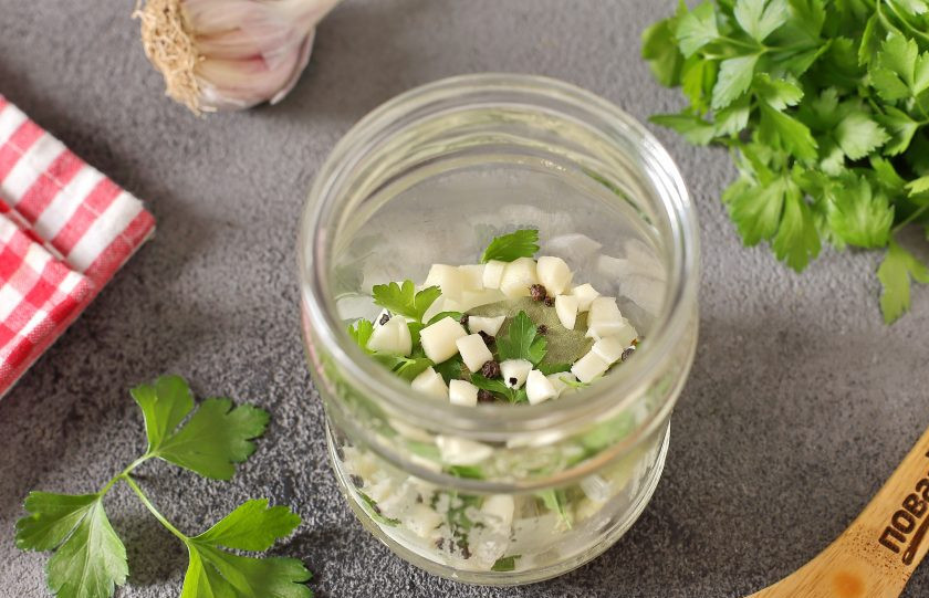 Маринованные кабачки с куркумой на зиму 1. Этап. Маринованные кабачки с куркумой на зиму: На дно чистой стерилизованной банки выложите измельченную петрушку, нарезанный кубиками чеснок, перец горошком, лавровый лист и нарезанный кольцами лук.