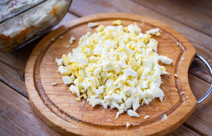 1. Этап. Салат Сельдь под одеялом: Отварные яйца почистите от скорлупы и мелко порубите ножом. Выложите порубленные яйца слоем.