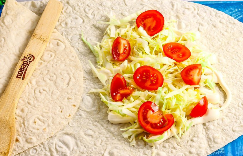 1. Этап. Шаурма с кебабом: В это время нарежьте капусту и присыпьте ее солью, протрите нарезку с нажимом, чтобы она выпустила сок. Разверните лист тонкого и длинного лаваша, смажьте его край майонезом, выложите на него капустную нарезку. Промойте помидоры черри и нарежьте их кружочками. Выложите на капусту.