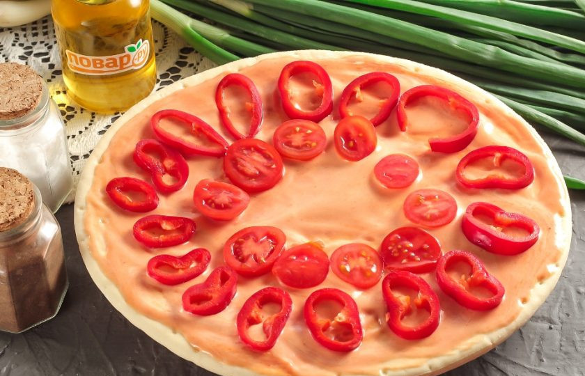 1. Этап. Болгарская пицца: Готовую основу для пиццы слегка разморозьте, смажьте кетчупом и майонезом. Промойте помидоры и болгарский перец, вырежьте сердцевинки и нарежьте кружочками. Выложите нарезки на основу.