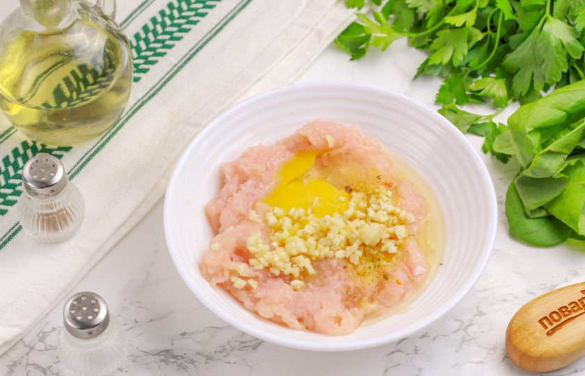 1. Этап. Кабачки с чесноком и фаршем: Первым делом приготовьте начинку. Для этого очищенный зубчик чеснока измельчите и добавьте в фарш вместе с универсальной приправой и яйцом. Тщательно все вымешайте.