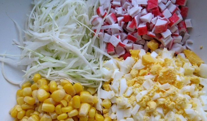 1. Этап. Салат Новогодняя елка: Крабовые палочки нарезаем кубиками. Капусту тонко шинкуем, яйца очищаем и измельчаем. Смешиваем все ингредиенты в салатнице, добавив кукурузу (без жидкости).