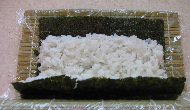 1. Этап. Ролл с лососем: 3. На специальный коврик для суши выкладываем лист нори, смачиваем его водой и выкладываем рис толщиной около 1 сантиметра, немного сворачиваем коврик, чтобы приподнять и перевернуть его на другую сторону.