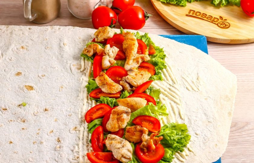 1. Этап. Курица в лаваше: Нарежьте промытые помидоры ломтиками, выложите на листья салата. По желанию можно добавить и нарезку свежего или соленого огурца. Сверху выложите обжаренные кусочки курицы.
