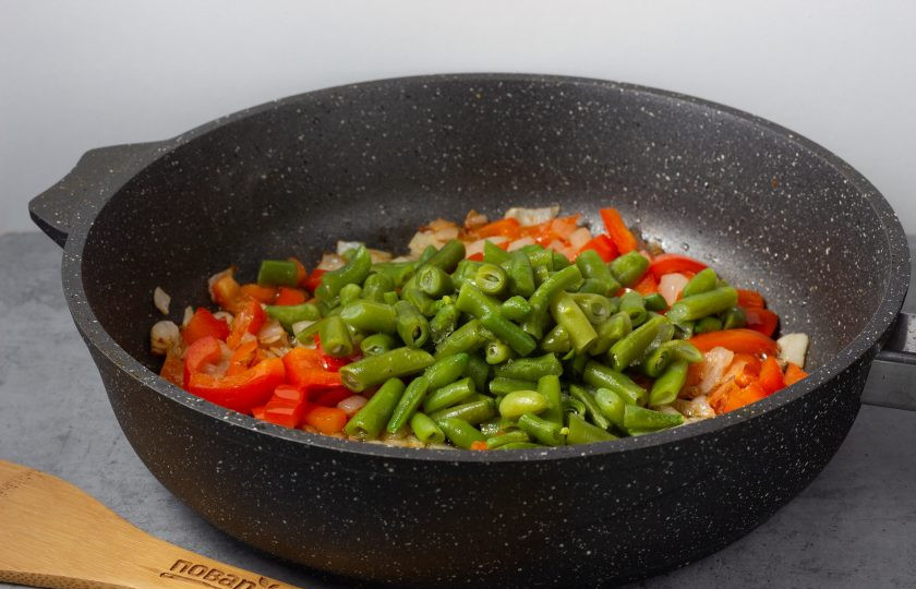 1. Этап. Теплый салат со стручковой фасолью и курицей: Перец немного обжарьте и добавьте фасоль. Жарьте всё вместе ещё 2-3 минуты.