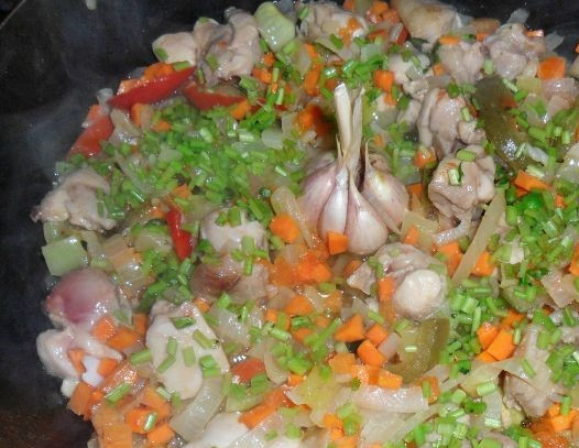 1. Этап. Испанская паэлья с курицей: 1. Замочите рис. Лук и морковь нарежьте небольшими кубиками. Возьмите болгарский перец нескольких цветов и мелко порежьте. Обжарьте лук на сковороде с разогретым маслом, добавьте морковь, сладкий перец. В центр сковородки положите целую, нечоищеную головку чеснока, порежьте петрушку и добавьте к овощам. Туда же отправьте нарезанную курицу. Тушите все 8-10 минут. Затем добавьте помидор, пропущенный через сито или мясорубку.