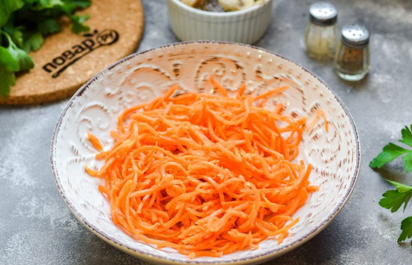 1. Этап. Салат с курицей и маринованными шампиньонами: Морковь по-корейски нарежьте, если она слишком длинная. Переложите морковь в салатник.