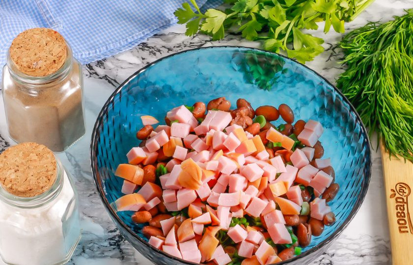 1. Этап. Салат с фасолью, сосисками, сыром и сухариками: Сосиски очистите от оболочки, нарежьте мелкими кубиками. Добавьте нарезку в емкость.