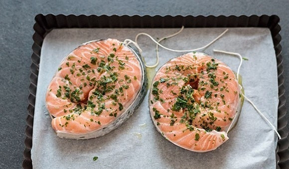 1. Этап. Лосось, запеченный с картофелем: 2. Положите рыбу на противень, покрытый пергаментом, и каждый ломтик рыбы сдобрите измельченным чесноком и петрушкой.